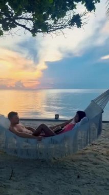 Hua Hin Tayland 'da tropik bir plajda güneşin doğuşunu izleyen bir çift kadın ve erkek. Huahin Tayland sahilindeki hamakta Asyalı kadınlar ve Avrupalı erkekler
