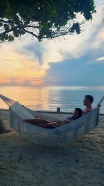 Hua Hin Tayland 'da tropik bir plajda güneşin doğuşunu izleyen bir çift kadın ve erkek. Huahin Tayland sahilindeki hamakta Asyalı kadınlar ve Avrupalı erkekler