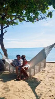 Hua Hin Tayland 'da tropik bir plajda güneşin doğuşunu izleyen bir çift kadın ve erkek. Huahin Tayland sahilindeki hamakta Asyalı kadınlar ve Avrupalı erkekler