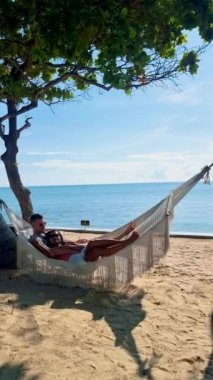Hua Hin Tayland 'da tropik bir plajda güneşin doğuşunu izleyen bir çift kadın ve erkek. Huahin Tayland sahilindeki hamakta Asyalı kadınlar ve Avrupalı erkekler