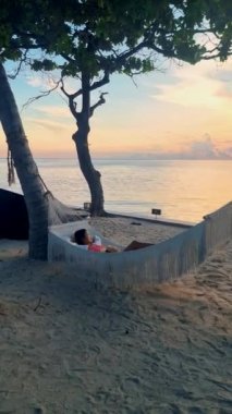 Hua Hin Tayland 'da bir hamakta güneşin doğuşunu izleyen kadınlar. Huahin Tayland sahilindeki hamakta yaşayan Asyalı kadınlar.