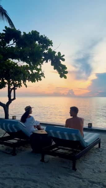 ビーチベッドの椅子 熱帯プール 海を見下ろすビーチでヤシの木があるプールでリラックスした男女のカップル — ストック動画
