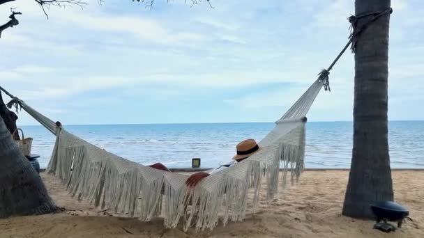 女性はホアヒンタイの熱帯ビーチでハンモックで日の出を見ています タイのハインビーチでハンモックでアジアの女性 — ストック動画