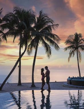 Birkaç erkek ve kadın plaj yataklarında havuzda dinleniyor sandalyeler, tropikal havuz ve okyanusa bakan palmiye ağaçları olan bir havuz.