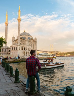 İstanbul Türkiye Haziran 2018, İstanbul Boğaz Köprüsü ve İstanbul 'da gün batımında Ortakoy Camisi. Turistler rıhtımda dinleniyor