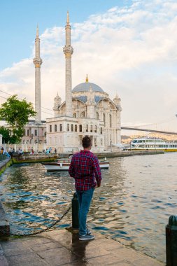 İstanbul Türkiye Haziran 2018, İstanbul Boğaz Köprüsü ve İstanbul 'da gün batımında Ortakoy Camisi. Turistler rıhtımda dinleniyor