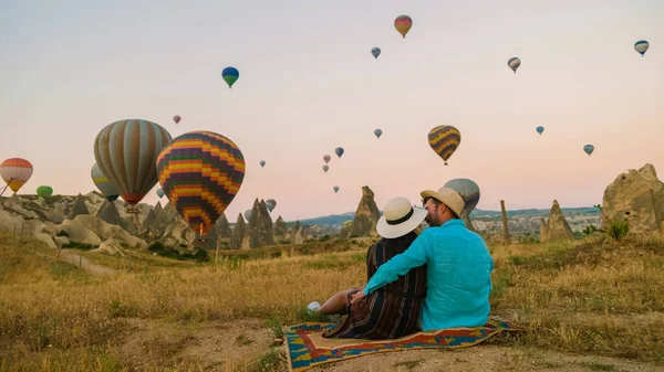 アジアの女性と白人男性中年カパドキヤカッパドキアへの旅行でトルコ 休暇中にカパドキヤカッパドキアトルコの熱気球を見ている日の出の間に幸せな若いカップル — ストック写真