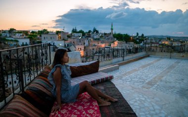 Ayvali Goreme Kapadokya 'nın tarihi bir köyünün çatısında içki içen mutlu çift, gün batımını izliyorlar Kapadokya.. 