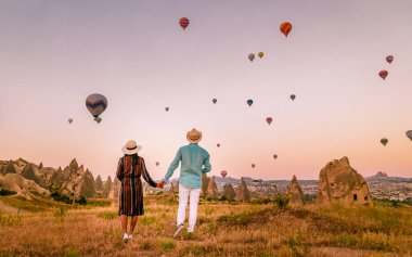 Asyalı kadınlar ve beyaz erkekler Kapadokya Kapadokya Türkiye 'ye seyahatlerinde, gün doğarken Kapadokya Kapadokya Türkiye' nin sıcak hava balonlarını izleyen mutlu genç bir çift