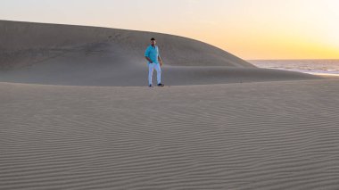 Maspalomas Gran Canaria İspanya sahillerinde yürüyen genç adamlar, Maspalomas Gran Canaria çölünde güneş doğarken kumlarda yürüyen genç adamlar.
