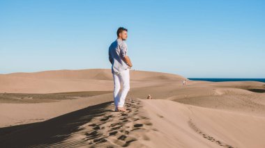 Maspalomas Gran Canaria İspanya sahillerinde yürüyen genç adamlar, Maspalomas Gran Canaria çölünde güneş doğarken kumlarda yürüyen genç adamlar.