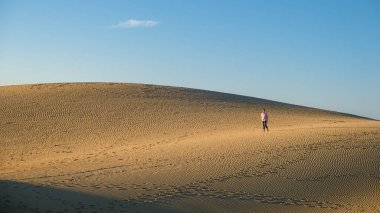 Maspalomas Gran Canaria İspanya sahillerinde yürüyen genç adamlar, Maspalomas Gran Canaria çölünde güneş doğarken kumlarda yürüyen genç adamlar.