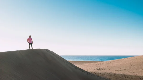 マスパロマス グラン カナリアのビーチを歩く若い男性スペイン マスパロマス グラン カナリアの砂漠で日の出の間に砂の中を歩く若い男性 — ストック写真