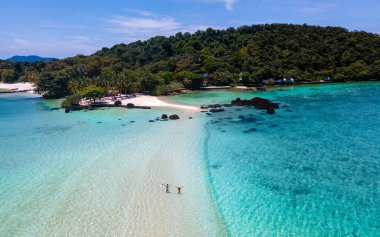 Tayland 'da tropik bir plajda, Koh Kham Trat' ta Koh Mak yakınlarında insansız hava aracı görüntüsü. Bir çift Asyalı kadın ve tropikal bir plajda beyaz erkek.