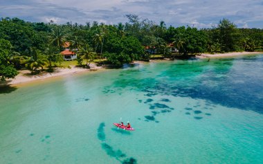 Erkekler ve kadınlar Koh Mak Tayland 'ın tropikal adasının okyanusunda Kayak' ta. Erkekler ve kadınlar mavi bir okyanusta kano ve palmiye ağaçlı beyaz plajda