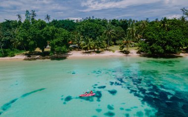 Erkekler ve kadınlar Koh Mak Tayland 'ın tropikal adasının okyanusunda Kayak' ta. Erkekler ve kadınlar mavi bir okyanusta kano ve palmiye ağaçlı beyaz plajda
