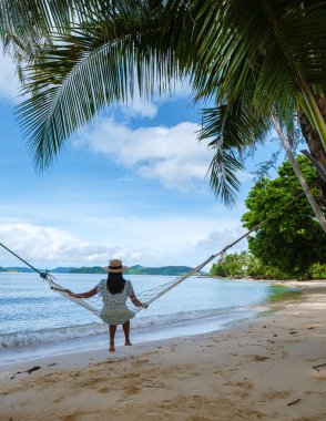 Asyalı kadınlar ve beyaz erkekler Koh Mak Tayland adasında palmiye ağaçlarıyla plajda dinleniyorlar. Palmiye ağaçları ve kumsalda beyaz kumlar 