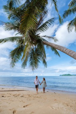 Asyalı kadınlar ve beyaz erkekler Koh Mak Tayland adasında palmiye ağaçlarıyla plajda dinleniyorlar. Palmiye ağaçları ve kumsalda beyaz kumlar 