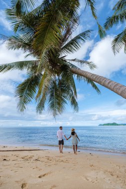 Asyalı kadınlar ve beyaz erkekler Koh Mak Tayland adasında palmiye ağaçlarıyla plajda dinleniyorlar. Palmiye ağaçları ve kumsalda beyaz kumlar 