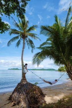 Asyalı kadınlar ve beyaz erkekler Koh Mak Tayland adasında palmiye ağaçlarıyla plajda dinleniyorlar. Palmiye ağaçları ve kumsalda beyaz kumlar 