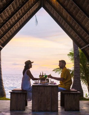 Koh Mak Tayland adasında gün batımında Tayland yemeğiyle sahilde romantik bir akşam yemeği. Birkaç erkek ve kadın sahilde romantik bir akşam yemeği yiyor.