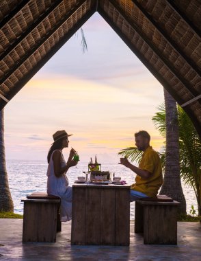 Koh Mak Tayland adasında gün batımında Tayland yemeğiyle sahilde romantik bir akşam yemeği. Birkaç erkek ve kadın sahilde romantik bir akşam yemeği yiyor.
