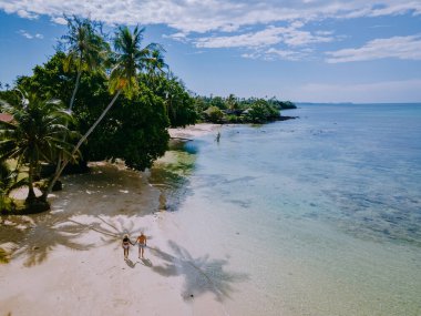 Tayland 'daki Koh Mak adasında tatilde olan iki erkek ve kadın. Tropik bir adada turkuaz renkli su ve palmiye ağaçları, insansız hava aracı görüntüsü