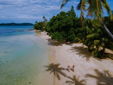 Tayland 'daki Koh Mak adasında tatilde olan iki erkek ve kadın. Tropik bir adada turkuaz renkli su ve palmiye ağaçları, insansız hava aracı görüntüsü