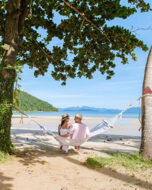 Erkekler ve kadınlar palmiye ağacının altındaki bir hamakta, Koh Mak tropik adası Tayland 'ın palmiye ağaçları arasındaki plajda dinleniyorlar..