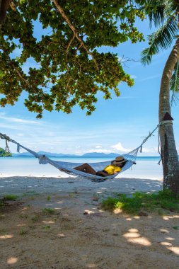 Sahildeki bir hamakta uyuyan Asyalı kadınlar Koh Mak tropik adası Tayland 'ın palmiye ağaçları arasındaki plajda hamak..