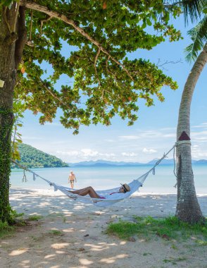 Erkekler ve kadınlar tropik bir plajda dinleniyorlar. Koh Mak tropik adası Tayland 'ın palmiye ağaçları arasındaki sahilde hamak..