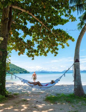 Erkekler ve kadınlar tropik bir plajda dinleniyorlar. Koh Mak tropik adası Tayland 'ın palmiye ağaçları arasındaki sahilde hamak..