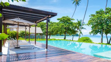 Koh Mak Tayland 2022, Tayland 'da güneşli bir günde tropikal okyanus manzaralı palmiye ağaçları olan lüks bir yüzme havuzu.