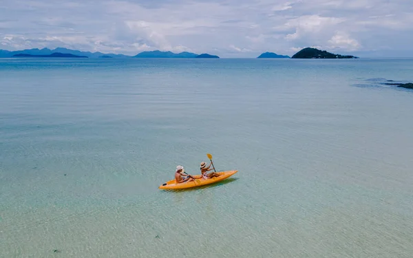 couple mid age men and women paddling in Kayak in the ocean of the tropical Island of Koh Mak Thailand. men and women in kayaks at a blue ocean and white beach with palm trees