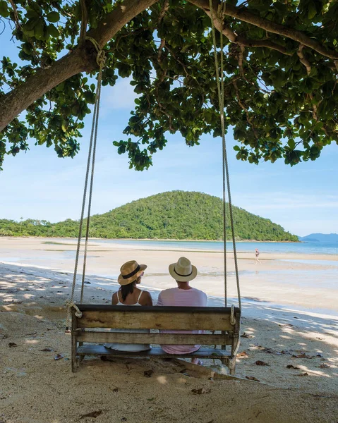 Men and women relaxing on a tropical beach on a swing bench. swing bench on the beach between palm trees of Koh Mak tropical Island Thailand.