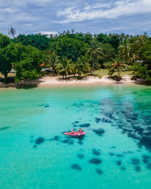 Erkekler ve kadınlar Koh Mak Tayland tropik adasının turkuaz renkli okyanusunda kano satıyorlar.