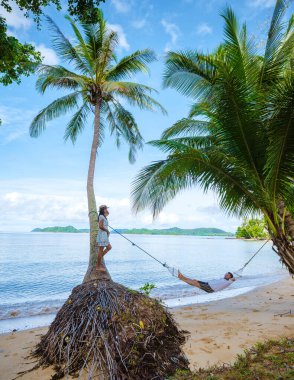 Tayland Koh Mak 'ta tropik bir adada tatil yapan birkaç erkek ve kadınla plajda hamak. Tropik bir adada turkuaz renkli su ve palmiye ağaçları, insansız hava aracı görüntüsü