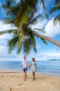 Tayland Koh Mak 'taki tropik bir adada, asılı bir palmiye ağacının altında yürüyen bir çift kadın ve erkek. Tropik bir adada turkuaz renkli su ve palmiye ağaçları, insansız hava aracı görüntüsü