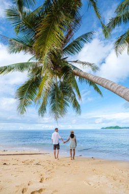 Tayland Koh Mak 'taki tropik bir adada, asılı bir palmiye ağacının altında yürüyen bir çift kadın ve erkek. Tropik bir adada turkuaz renkli su ve palmiye ağaçları, insansız hava aracı görüntüsü