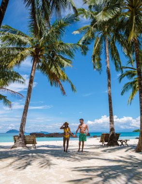 Koh Kham Trat Tayland, beyaz tropik bir plajda yüzme elbiseli palmiye ağaçlarıyla yürüyen birkaç kadın ve erkek.