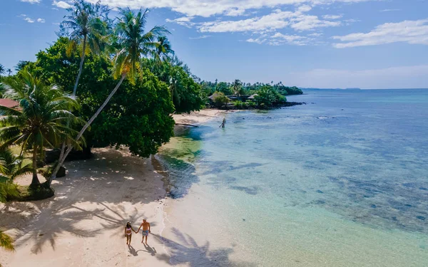 Palmiye ağaçlı tropik plaj, Tayland 'da Koh Mak' ta tropik bir adada tatil yapan birkaç erkek ve kadın. Tropik bir adada turkuaz renkli su ve palmiye ağaçları, insansız hava aracı görüntüsü
