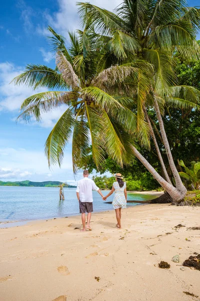 タイの熱帯の島で休暇中にぶら下がったヤシの木の下を歩いている男女のカップル 熱帯の島のターコイズブルーの水とヤシの木無人航空機の眺め — ストック写真
