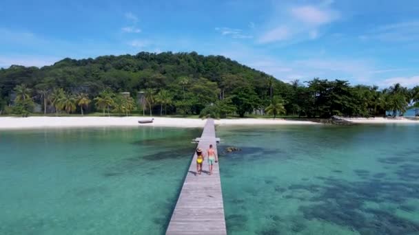 トラット Koh Kham Trat Thailand タイのコマック島付近の熱帯島 ヤシの木の白い砂浜 木の板の上を歩く男女のカップル — ストック動画