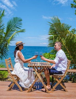 Günbatımında okyanus cephesinde şarap içen çift, okyanus sahilinin terasında kadın ve erkek. Erkekler ve kadınlar tatilde içki içiyorlar.