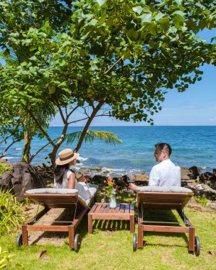 Tatil sırasında okyanusta bir içkiyle rahatlayan çift, erkekler ve kadınlar okyanus kenarındaki sahil yataklarında dinleniyorlar.. 