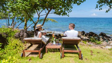 Tatil sırasında okyanusta bir içkiyle rahatlayan çift, erkekler ve kadınlar okyanus kenarındaki sahil yataklarında dinleniyorlar.. 