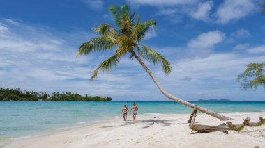 Koh Kood Tayland adasında tatilde olan iki erkek ve kadın. Beyaz tropikal sahilde palmiye ağaçları sallanıyor. Mavi okyanusta birkaç erkek ve kadın Tayland 'da tatilde.