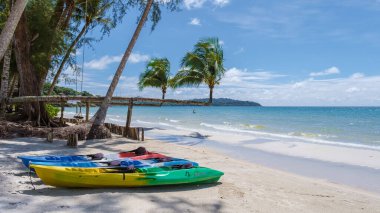 Koh Kood Tayland adasında palmiye ağaçları olan tropik bir sahil. Mavi okyanuslu, beyaz tropikal sahilde asılı palmiye ağaçları, kumsalda renkli kanolar.