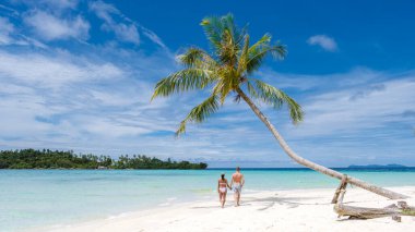 Koh Kood Tayland adasında palmiye ağaçları olan tropik bir sahil. Beyaz tropikal sahilde palmiye ağaçları sallanıyor. Mavi okyanusta birkaç erkek ve kadın Tayland 'da tatilde.