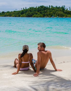 Sahilde oturan Asyalı kadınlar ve tropik bir adada palmiye ağaçları olan Koh Kood Tayland 'da beyaz erkekler.. 